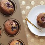 blueberry muffin on a plate next to tray of blueberry muffins