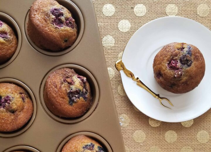 blueberry muffin on a plate next to tray of blueberry muffins