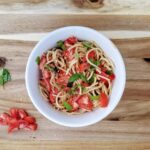 fresh summer tomato pasta with basil in a white bowl on a wooden board