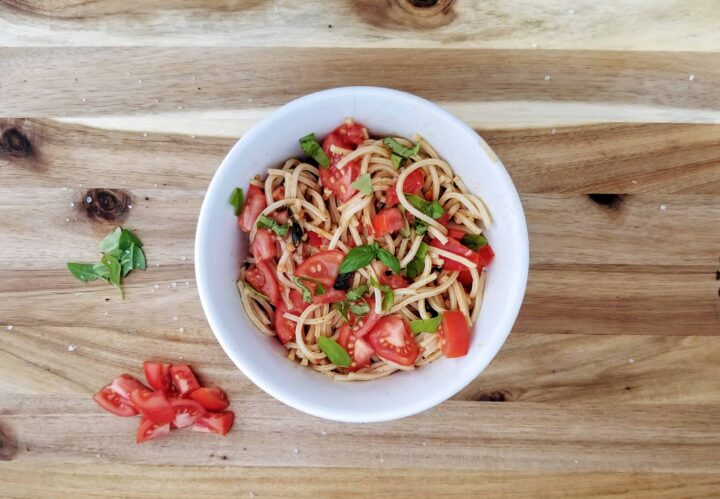 fresh summer tomato pasta with basil in a white bowl on a wooden board