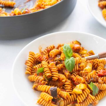 white bowl of roasted ratatouille ragu on rotini pasta with fresh basil