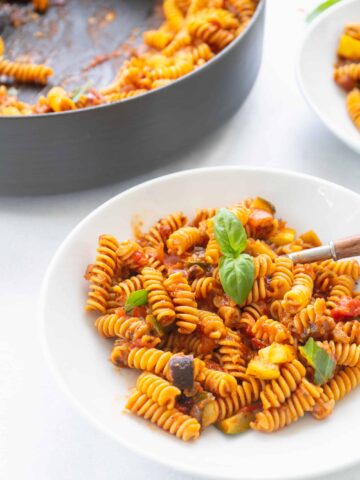 white bowl of roasted ratatouille ragu on rotini pasta with fresh basil
