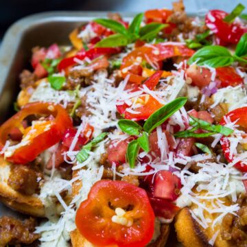 Take game day to another level with these delicious Italian Nachos with Spicy Sausage and Pesto Alfredo. They're everything you love about nachos, but they'd make any Nonna proud! Toasted bread is topped with spicy Italian sausage, tomato and cherry pepper relish and pesto alfredo! Make a big pan and watch them disappear! | Sip and Spice #gameday #nachos #Italian #pestoalfredo #snacks #dinner