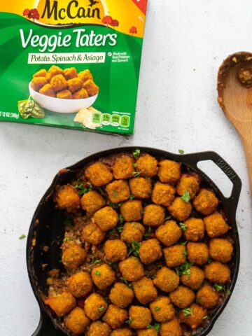 shepherd's pie in a cast iron skillet with tater tots on top with mccain tater tot packaging on the side