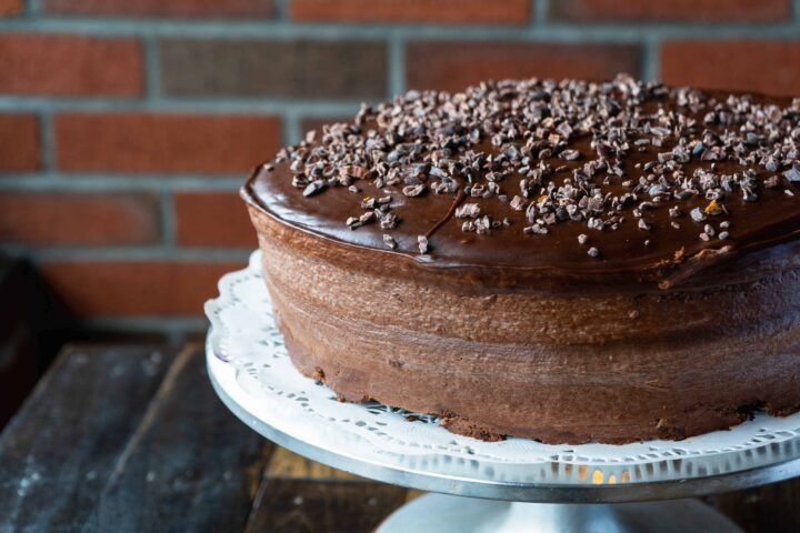 chocolate cake on a cake stand in front of an exposed brick wall